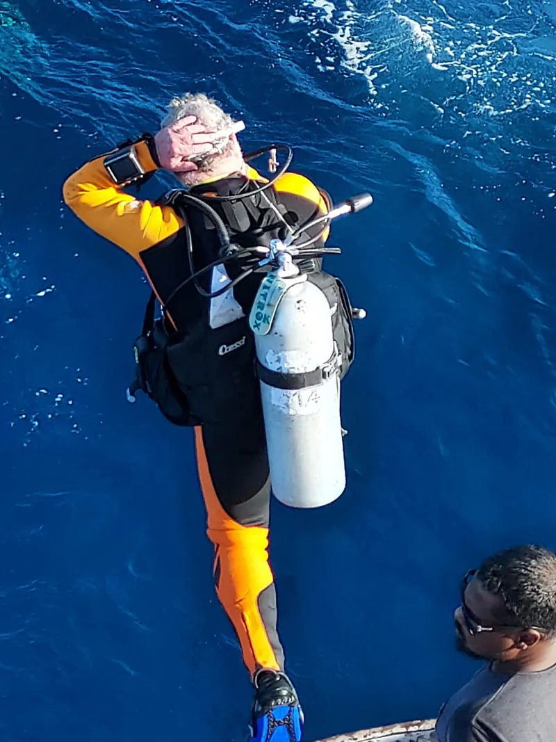 Person in Tauchausrüstung beim Sprung vom Boot ins blaue Meer.